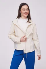 Campera liviana color crema con capucha, cierre frontal completo y cordones ajustables en el cuello y el ruedo. Cuenta con mangas largas con puños elásticos y bolsillos laterales.