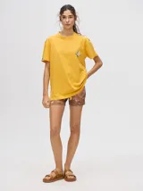 Remera de corte cuadrado y ajuste holgado, color verde oliva, con pequeño estampado gráfico de un velero en el pecho y etiqueta decorativa en la manga.