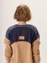 Buzo de manga larga con diseño color block. Cuerpo principal color camel, sección central de la espalda color azul marino liso y hombros con tejido de lana texturado en tonos azules. Posee un parche de cuero marrón con el logo grabado en la espalda.