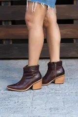 Botas cortas de cuero color marrón oscuro, con diseño estilo western, taco cuadrado de madera y punta fina.