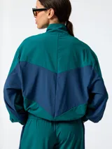 Campera cortaviento de microfibra oversize verde con inserciones azul marino en los costados y mangas, cuello alto y cierre frontal con cremallera.