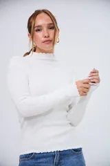 Polera blanca de manga larga, con cuello alto y bordes ondulados en el cuello y el dobladillo.