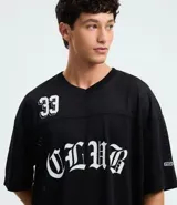 Remera masculina negra de estilo sportcore, modelo boxy con cuello en V y manga corta. Presenta textura "furadinha" (perforada), estampado numeral "33" en el hombro y "CLUB" en el pecho, ambos en blanco con tipografía gótica.