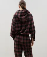 Camisa de manga larga con capucha, confeccionada en tejido liviano con estampado a cuadros. Presenta cierre frontal con botones y lazo regulable en la cintura.
