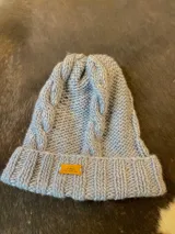 Gorro tejido en lana merino de color celeste, con diseño de trenzas frontales, vuelta acanalada y etiqueta frontal con logo.