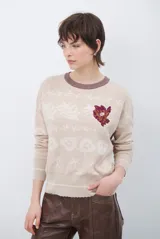 Buzo de tejido de punto en color beige con estampado de motivos florales y abstractos en tonos marrones. Presenta cuello redondo con borde en color azul vibrante, mangas largas y puños ajustados.