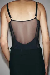 Body de escote corazón con aros y tirantes finos ajustables. Presenta un diseño con paneles de tejido opaco y transparencias laterales. Cierre inferior con botones a presión.