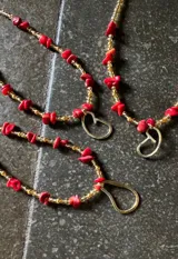 Collar de cuentas doradas y rojas con dije en forma de lágrima.