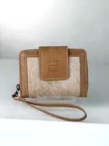 Billetera pequeña de cuero color marrón claro con paneles frontales de pelo natural. Presenta un cierre de solapa con broche y un logo grabado de un búho. Incluye una correa de muñeca extraíble.