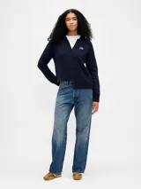 Buzo tipo polo de tejido de punto, color azul marino, con cuello solapa, escote en V y logo de la marca bordado en el pecho. Presenta mangas largas y un diseño de ruedo asimétrico con detalle acanalado.