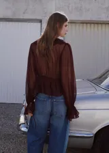 Blusa fluida color bordó, con escote en V, mangas largas con volantes en los puños y detalles de volantes en el frente y el cuello.