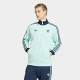 Campera deportiva Adidas Originals de la selección de Alemania, color verde agua con detalles en azul marino. Presenta cuello alto, cierre frontal completo, bolsillos laterales y las icónicas tres tiras de la marca en las mangas. Incluye el logo del trébol y el escudo de la federación alemana en el pecho.