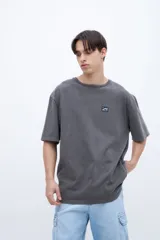 Remera blanca de algodón con calce oversize, teñida en prenda, con parche chico en el pecho y diseño fotográfico de dos tragos en la espalda.