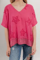 Blusa lila de algodón con escote en V, mangas cortas y holgadas. Presenta estrellas bordadas en relieve en la parte superior y un borde de lentejuelas en el dobladillo inferior.