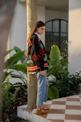 Cárdigan negro de tejido de punto con bordados de rosas rojas y hojas verdes. Presenta detalles bordados multicolores en hombros y puños.