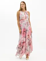 Vestido largo de fiesta con estampado floral en tonos rosa y gris sobre fondo blanco. Presenta cuello halter con abertura tipo lágrima, cintura drapeada y falda amplia con capas asimétricas y bajo en picos. Confeccionado en tejido ligero con forro interior.