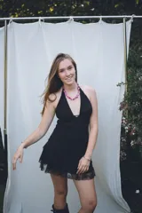 Vestido corto negro con escote en V profundo, estilo halter con tiras para atar al cuello. Presenta un diseño ajustado en el busto con tiras ajustables bajo el mismo que se cruzan y anudan en la espalda, y falda con volado en el ruedo con detalle de encaje.