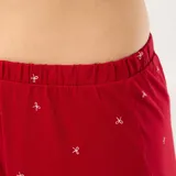 Conjunto de pijama de dos piezas confeccionado en tejido jersey color rojo con estampado de pequeñas cruces blancas. La parte superior consiste en una camisa de manga larga con cuello de solapa y cierre frontal de botones, mientras que la parte inferior es un pantalón largo de corte recto.