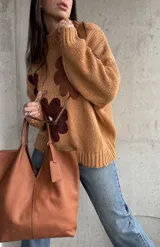 Sweater de punto grueso color camel, con diseño de flores grandes aplicadas en tonos marrones y centro crema. Presenta cuello redondo alto, mangas largas con hombros caídos y terminaciones acanaladas.