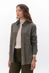 Camisa beige de manga larga, con cuello clásico, botones marrones y dos bolsillos frontales. Presenta costuras decorativas en contraste.