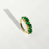 Anillo dorado con detalle de cristales en forma de corazón color verde esmeralda.