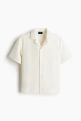 Camisa de manga corta con cuello abierto, confeccionada en tejido de punto con textura. Presenta un diseño de corte regular con tapeta lisa y bajo recto.