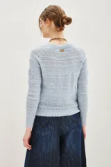 Cardigan de punto calado en color beige, con escote en V y cierre frontal de botones. Presenta un diseño de textura con franjas horizontales y mangas largas.