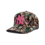 Gorro trucker con estampado de camuflaje de bosque, visera curva y cierre trasero ajustable. Presenta un aplique bordado en relieve con las letras "NY" en color fucsia en el centro, acompañado de los textos bordados "Mi Casa" y "Su Casa" a los lados.