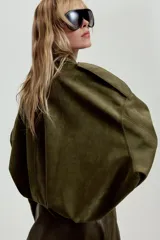 Chaqueta de efecto ante color marrón claro, con cuello solapa, manga larga con trabillas en los hombros y bajo abullonado. Cierre frontal con cremallera y botones ocultos por solapa.