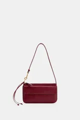 Bolso de hombro color bordó, con asa de hombro, bolsillo exterior con solapa y cierre de imán, y cierre principal con cremallera. Incluye detalle de anilla metálica dorada y tira con nudos en el lateral.