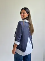 Sweater de punto azul con diseño asimétrico y detalles bordados, que incluye una bufanda a juego y una camisa blanca de lino debajo.