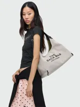 Cartera tipo hobo de Marc Jacobs, confeccionada en lona color beige con detalles en cuero negro. Presenta el logo estampado en el frente y una correa de hombro ajustable.