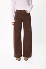 Jean de corte wide leg en color marrón chocolate, con tiro medio y cierre frontal con botón y cremallera. Presenta un diseño de cinco bolsillos y costuras visibles.