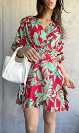 Vestido corto de corte cruzado con estampado de hojas verdes sobre fondo rojo, mangas 3/4 y volantes en el ruedo.