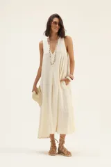 Vestido largo color crudo, de lino, con escote en V, corte acampanado y bolsillos laterales.