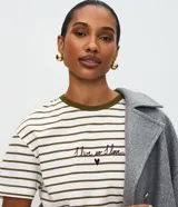 Remera de corte boxy fit, con diseño a rayas horizontales en color blanco y verde oliva. Presenta cuello redondo en contraste, mangas cortas y un bordado frontal con la frase 'I live so I love' acompañada de un pequeño corazón.