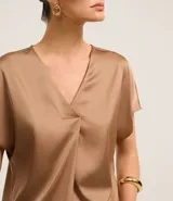 Blusa color café confeccionada en poliéster y elastano, con acabado satinado, escote V y mangas cortas. Presenta pliegues delanteros.