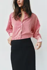 Camisa de cuello solapa y manga larga con rayas verticales rojas y blancas, con puños anchos blancos contrastantes y cierre frontal de botones.