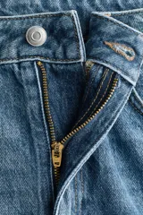 Jean de tiro alto y corte baggy, confeccionado en denim de algodón rígido en tono azul medio con efecto deslavado. Presenta diseño de cinco bolsillos, trabillas para cinto y cierre frontal con botón y cremallera.