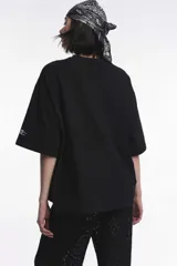 Remera blanca de corte boxy, cuello redondo a la base y mangas cortas. Presenta un pequeño estampado localizado en el centro del pecho que simula un ají en tono rojizo.