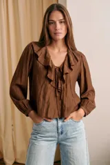 Blusa de color marrón con acabado satinado, cuello en V con volados y lazo de ajuste frontal. Presenta mangas largas con puños elásticos y un corte holgado.