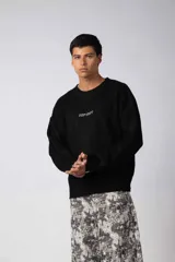 Sweater de punto acanalado con diseño de calce relajado, cuello redondo y mangas largas. Presenta una estampa gráfica pequeña en el centro del pecho y un parche con logo en el puño.