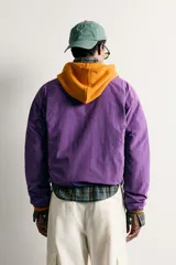 Chaqueta canguro técnica de corte relaxed fit en color violeta, con cuello subido ajustable, cierre frontal de cremallera parcial, manga larga y bolsillos frontales con cierre y tipo canguro.