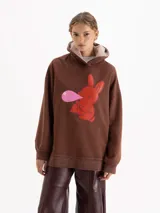 Buzo marrón de corte amplio con capucha forrada en corderito. Presenta una estampa frontal de un conejo rojo haciendo una burbuja de chicle, parte de la cápsula Il Bunny Porta Fortuna.