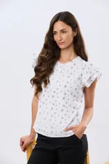 Blusa blanca sin mangas con volados en los hombros, cuello redondo con aberturas y cierre frontal parcial con botones.