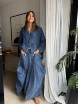 Pollera larga de jean fino color azul, de diseño amplio con gran movimiento y caída. Cuenta con elástico en la cintura, bolsillos delanteros aplicados, y detalles laterales de pinzas y sobretelas que aportan volumen.