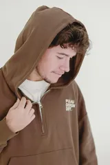 Canguro beige con capucha, cierre frontal parcial y bolsillo tipo canguro. Presenta estampado con texto en el pecho y detalle en la manga.