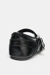 Zapato tipo bailarina de acabado acharolado en color negro, con punta redonda y suela plana. Presenta una tira ajustable con hebilla metálica y bandas elásticas cruzadas en el empeine.