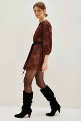 Vestido corto de estilo camisero con estampado animal print en tonos caramelo y negro. Presenta cuello en V con solapas negras, mangas tres cuartos y un lazo negro ajustable en la cintura para entallar la silueta.