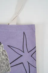 Bolso tote de tela con estampado de rayas verticales rosadas y blancas, laterales y asas en color beige. Presenta la palabra "BONJOUR" en verde en el centro y "INDIAN" en la parte inferior.